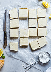 Cubes of butter or cheese arranged in a rectangular shape with one cube missing from array. Lemons on the upper right and lower left corner with a measuring cup with flour. 